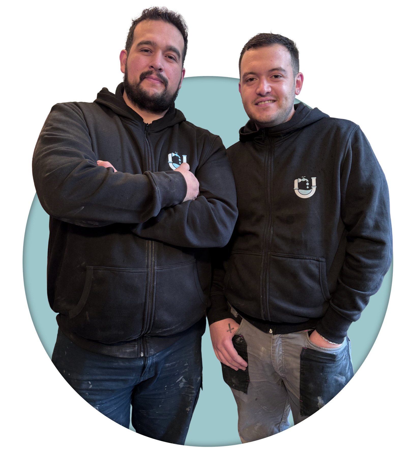 Dos personas de pie, ambas con sudaderas negras con un logotipo en el pecho, sobre un fondo azul claro.